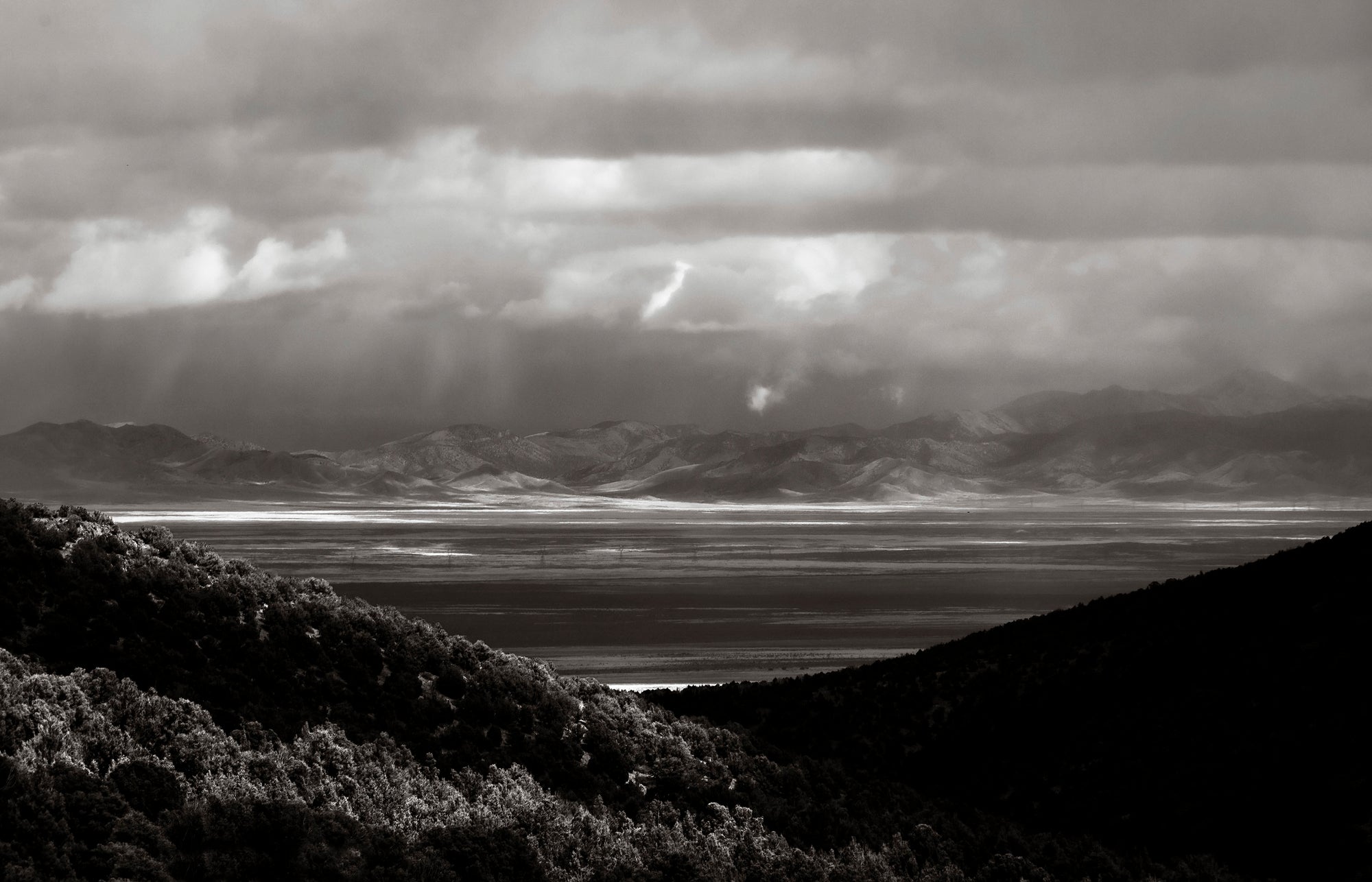 Black and white photograph of dramatic storm light breaking across the Onaqui Mountains beneath sweeping clouds in Utah by Ximena Echeverria