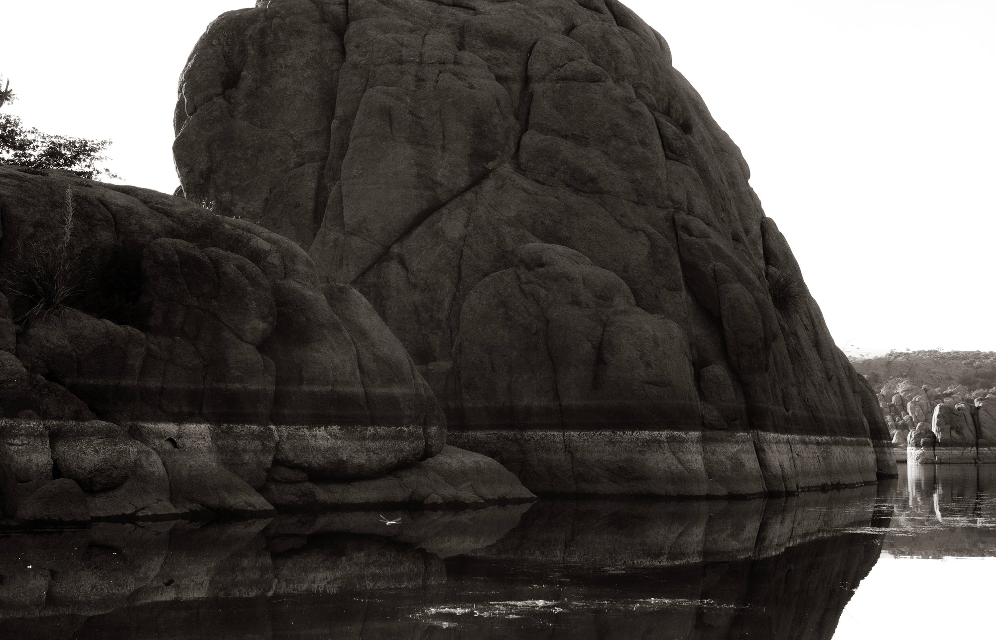 Black and white photograph of a massive granite boulder reflected in the calm waters of Watson Lake, Arizona by Ximena Echeverria